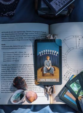 An artistic flat lay of tarot cards and astrology on a book with seashells, featuring Kupa Dokuzlusu card.