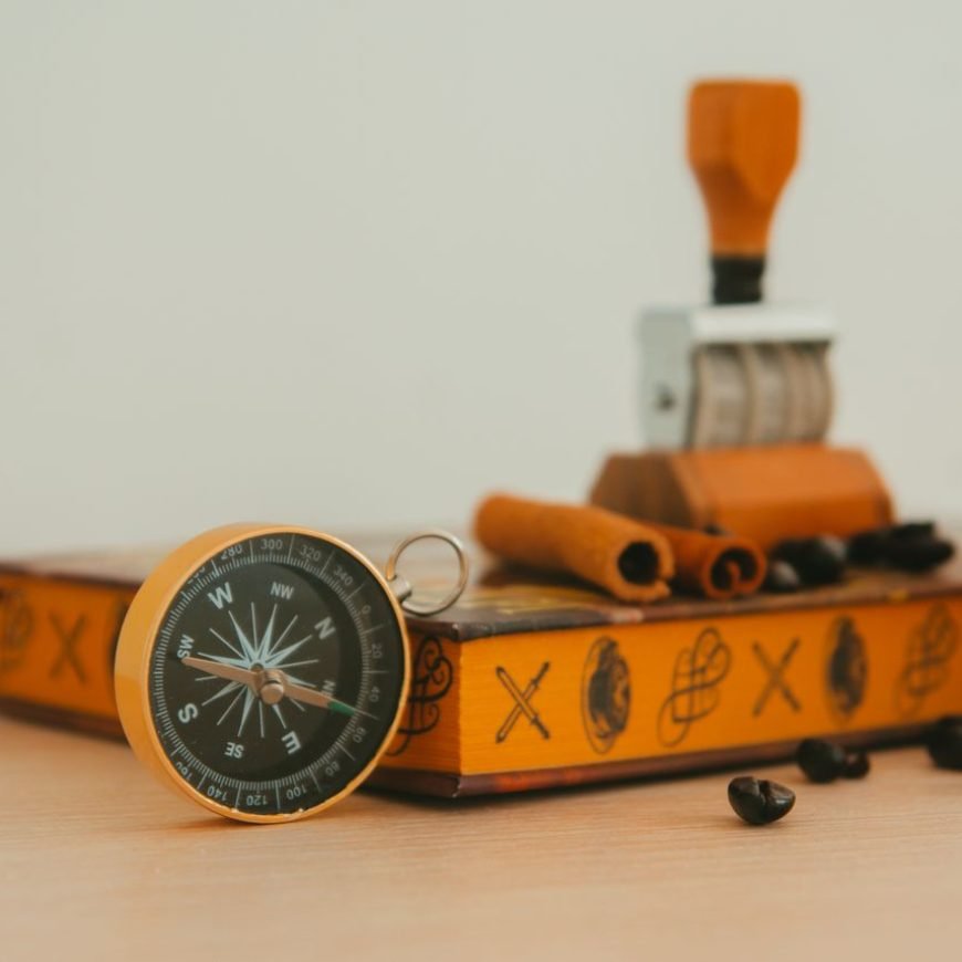 A vintage compass and stamp on a decorated box with coffee beans and cinnamon sticks, offering a warm, nostalgic vibe.